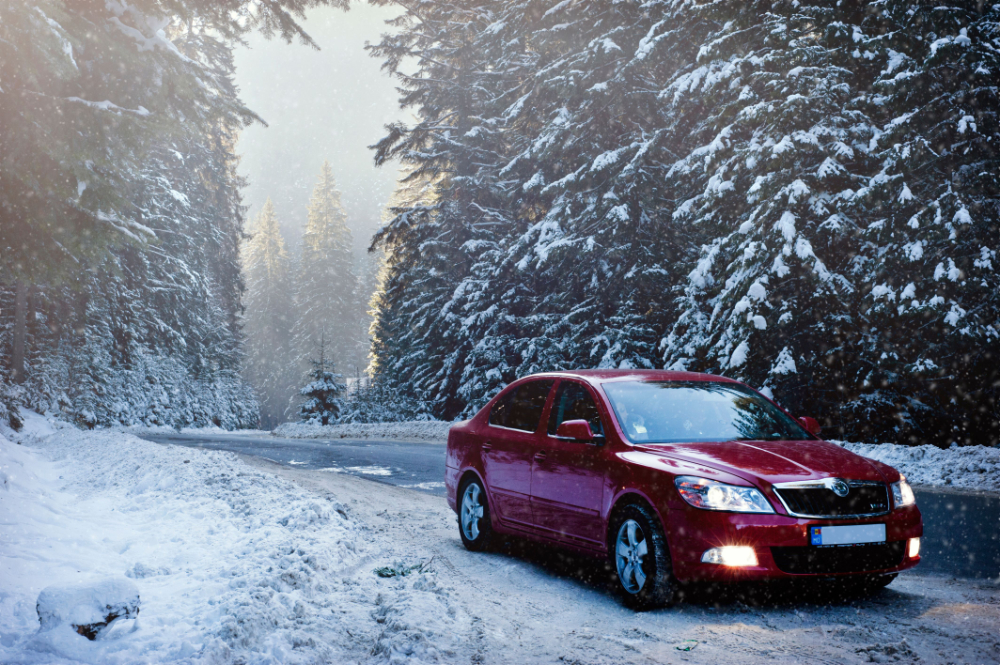 A red car drives along a snowy forest road in winter, surrounded by frosty trees